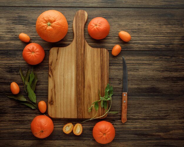 Top view of cutting board with orange tangerine kumquat knife around on wooden background