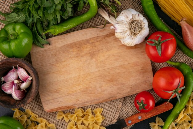 Top view of cutting board with tomatoes garlic bell and hot peppers and onions with mint on a beige napkin