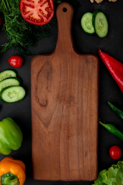 Top view of cutting board with vegetables as fennel tomato cucumber pepper around on black background