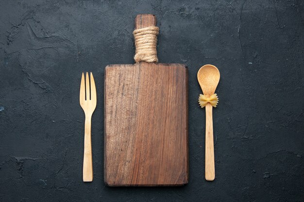 Top view cutting board wooden spoon and fork on dark surface