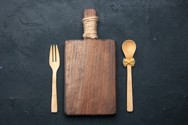 Top view cutting board wooden spoon and fork on dark surface