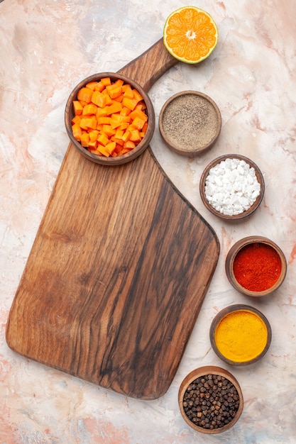 Top view cutting carrot in bowl on cutting board different spices in small bowls on nude surface