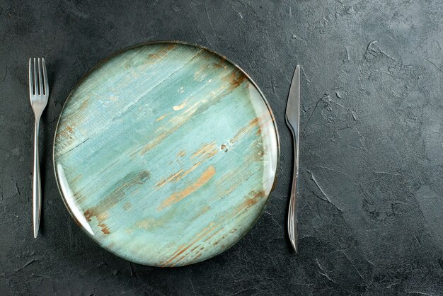 Top view cyan round plate fork and knife on dark surface copy place