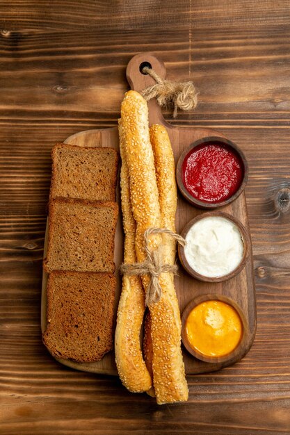 Вид сверху темные буханки хлеба с булочками и приправами на коричневом столе еда хлебная булочка острая
