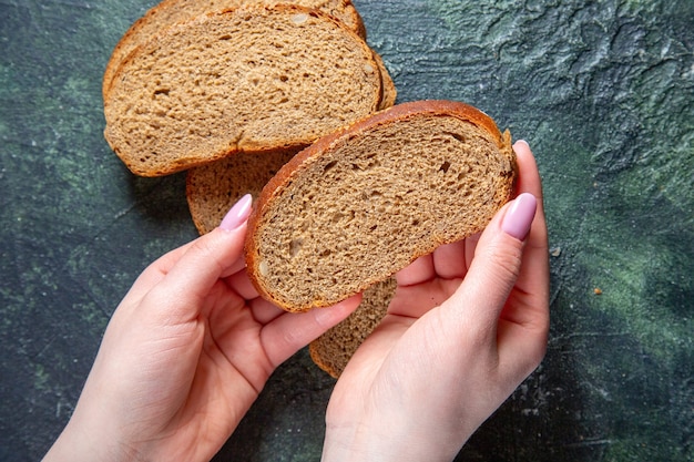 Вид сверху на темные буханки хлеба с женскими руками на темном столе