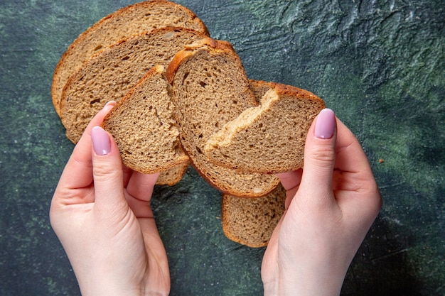 Foto gratuita pagnotte di pane scuro vista dall'alto con strappo femminile sulla scrivania scura