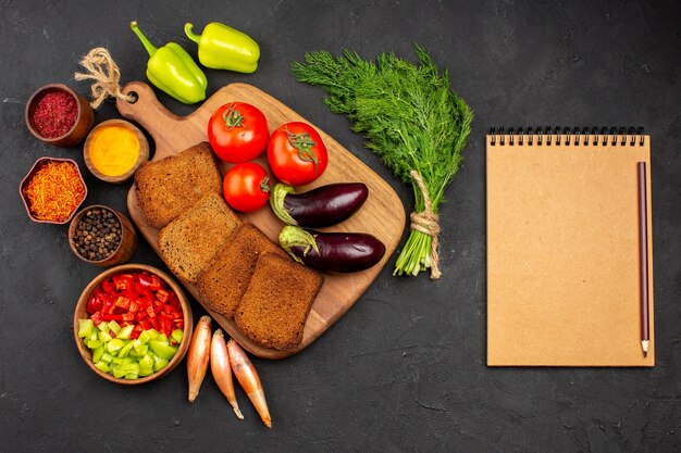 Вид сверху темные буханки хлеба с приправами, помидорами и баклажанами на темном фоне, салат, здоровье, спелая еда, овощная диета