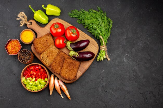 Вид сверху темные буханки хлеба с приправами, помидорами и баклажанами на темном фоне, салатом, здоровой спелой едой