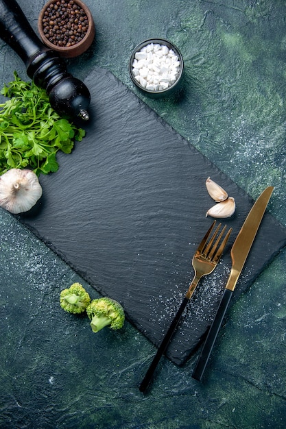 top view dark cutting board with seasonings cutlery and greens on blue surface color fork ripe salad meal