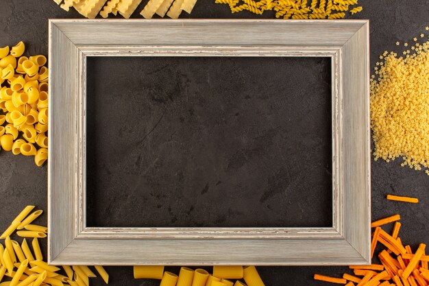 A top view dark photo frame along with different formed yellow raw pasta isolated on the dark