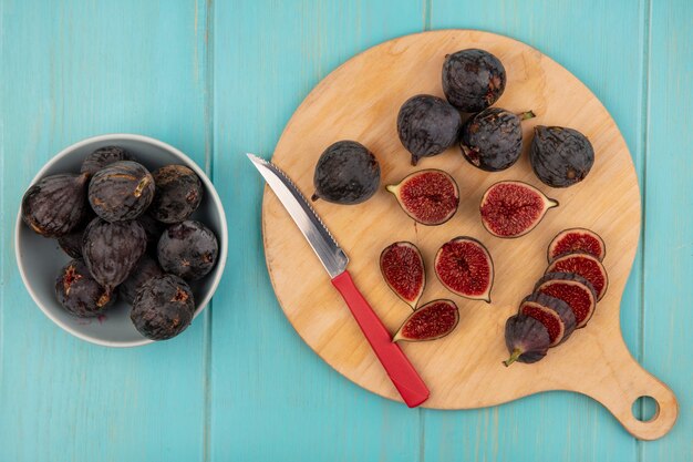 Top view of dark purple mission figs on a wooden kitchen board black figs on a bowl with knife on a blue wooden wall