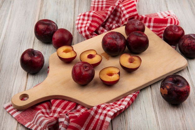 Top view of dark red half and whole pluots isolated on a wooden kitchen board on a checked cloth on a grey wooden surface