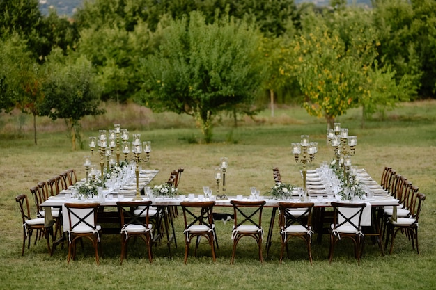 Top view of decorated with minimal floral bouquets and candles wedding celebration table with chiavari seats outdoors in the gardens in front of fruits trees