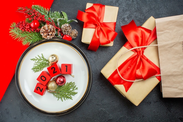 Free photo top view of decoration accessories numbers on a plate and beautiful gifts fir branches conifer cone on a dark table