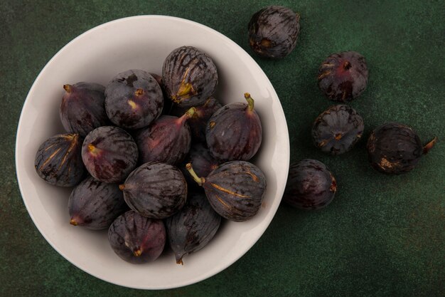 Top view of deep purple sweet mission figs on a bowl on a green surface