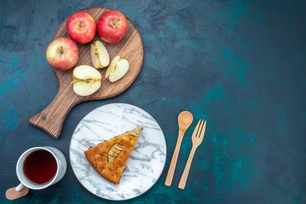 Top view delicious apple pie sliced inside plate with tea and apples on dark-blue desk fruit cake pie sugar sweet