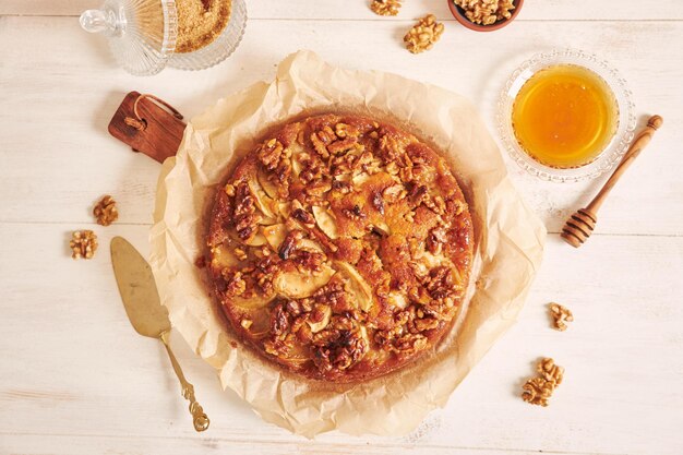 Top view of a delicious apple walnut cake with honey surrounded by ingredients on a white table