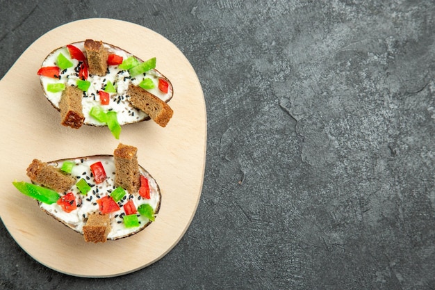 Top view of delicious avocado meal with sour cream sliced peppers and bread pieces on dark grey surface