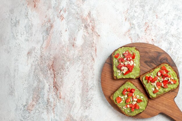 Top view of delicious avocado sandwiches with sliced red tomatoes on a white surface