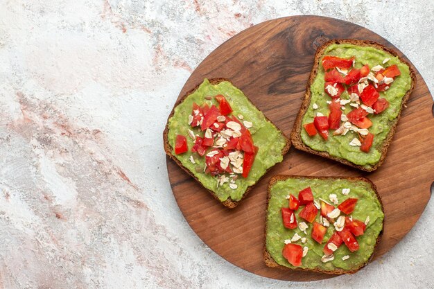 Top view of delicious avocado sandwiches with sliced red tomatoes on the white surface