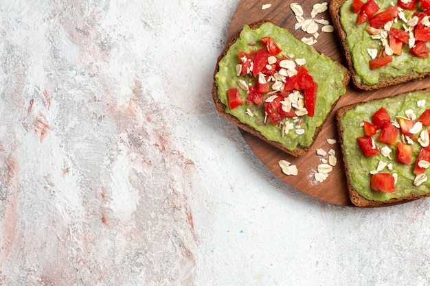 Top view of delicious avocado sandwiches with sliced red tomatoes on white surface