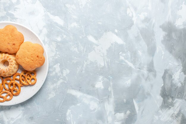 Top view delicious bagels with cookies and cakes inside plate on light white desk.