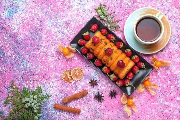 Top view delicious baked cake inside black cake pan with fresh red strawberries and cup of tea on the pink desk.