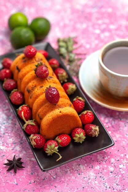 Вид сверху вкусный испеченный торт внутри черной формы для торта со свежим красным чаем клубники и лимонами на розовом столе.