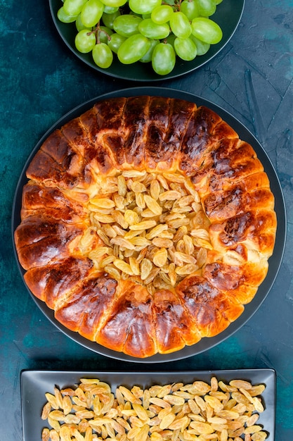 Vista dall'alto una deliziosa torta al forno con uvetta e uva verde fresca sull'impasto di biscotti dolci con torta di superficie blu scuro