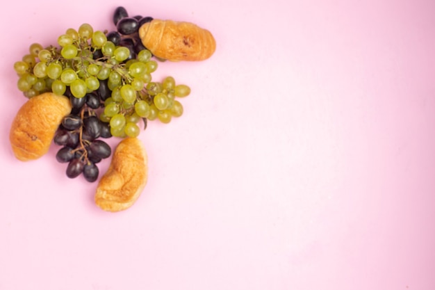 Top view delicious baked croissants with fruit filling along with fresh black and green grapes on pink desk