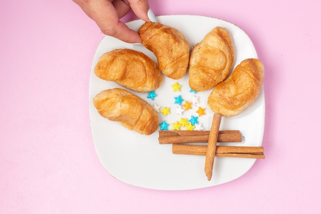 Vista dall'alto deliziosi croissant al forno con ripieno di frutta all'interno con caramelle alla cannella sulla scrivania rosa