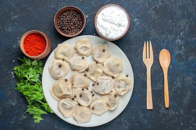 Top view of delicious baked dumplings inside plate along with pepper yogurt and greens on dark, dough meal food dinner meat calories