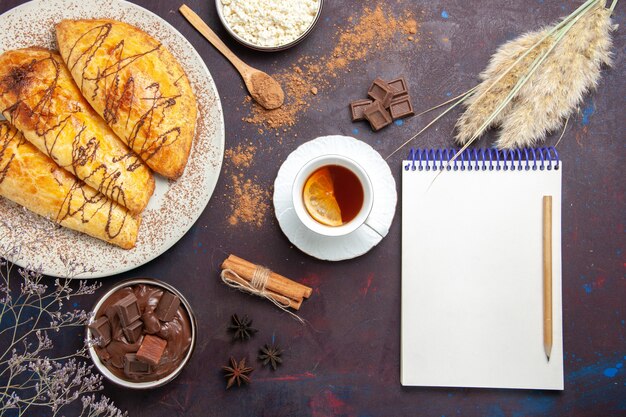 Top view delicious baked pastries with cottage cheese and tea on dark desk