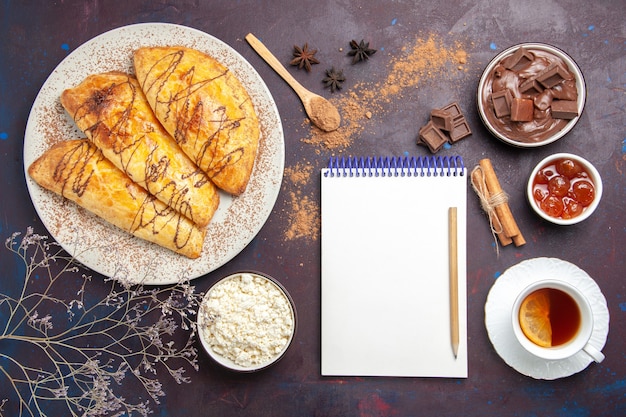 Vista dall'alto deliziosi pasticcini al forno con una tazza di tè e ricotta su uno spazio buio