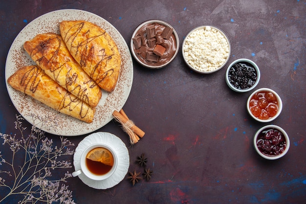 Vista dall'alto deliziosi pasticcini al forno con una tazza di marmellata di tè su uno spazio buio