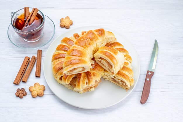 top view of delicious baked pastry with sweet filling sliced and whole along with cookies and tea on light desk, cookie biscuit pastry cake tea