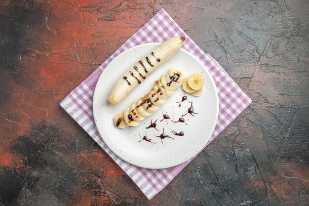 Top view delicious banana with sliced pieces inside plate on dark background