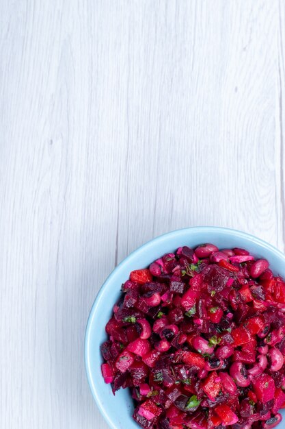 top view of delicious beet salad sliced with greens and vegetables inside blue plate on light desk, vegetable vitamine food meal health salad