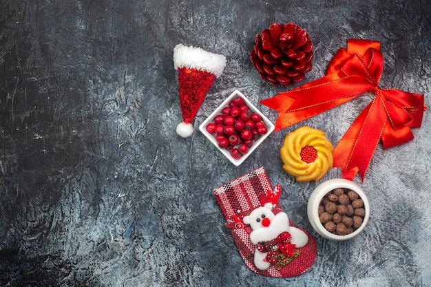 Вид сверху вкусного печенья и шоколада с кизилом в белых горшках новогодний носок красный конус хвойных деревьев красная лента с левой стороны на темной поверхности