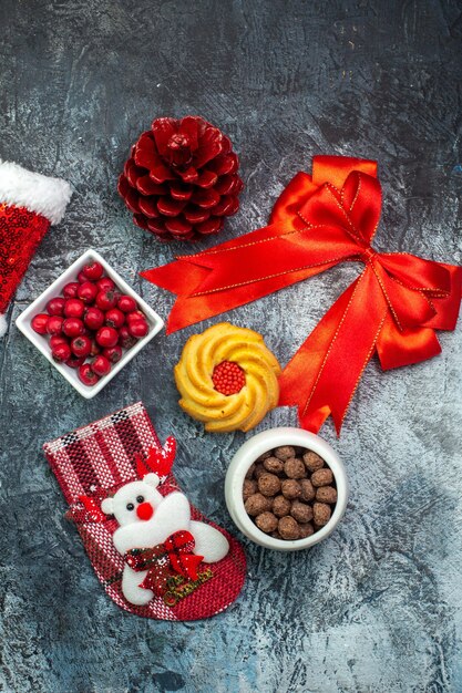 Вид сверху вкусного печенья и кизила на белой тарелке, новогодний носок, красный конус хвойных деревьев, красная лента, шляпа санта-клауса на темной поверхности