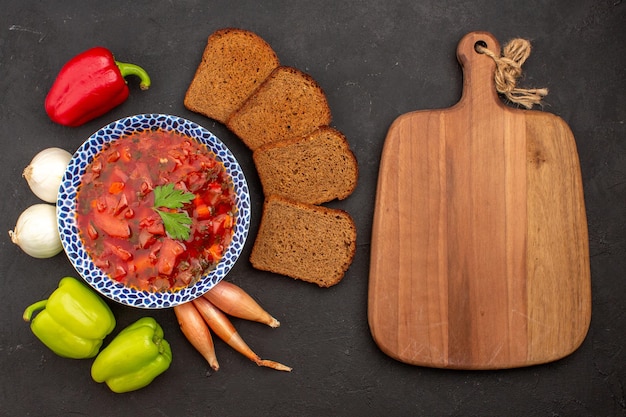 Вид сверху вкусного борща со свежими овощами и буханками хлеба на темном пространстве