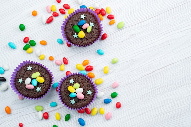 A top view delicious brownies inside purple forms with colorful candies on white, candy color sweets