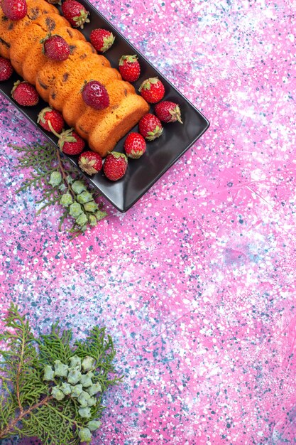 Top view delicious cake inside black cake pan with fresh red strawberries on the pink desk.