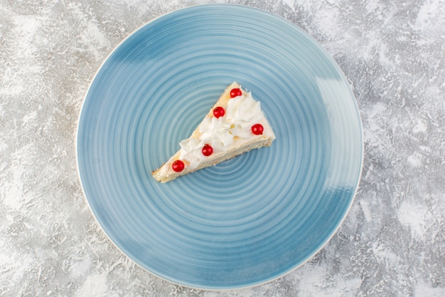Вид сверху вкусный кусочек торта внутри синей круглой тарелки со сливками и красными фруктами на сером фоне бисквитный торт чай сладкий