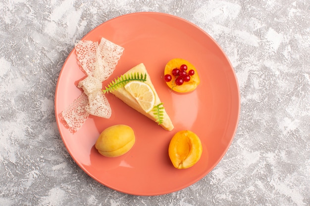 Top view delicious cake slice with apricot slice and fresh apricots inside peach plate on the light desk cake biscuit sugar sweet dough bake