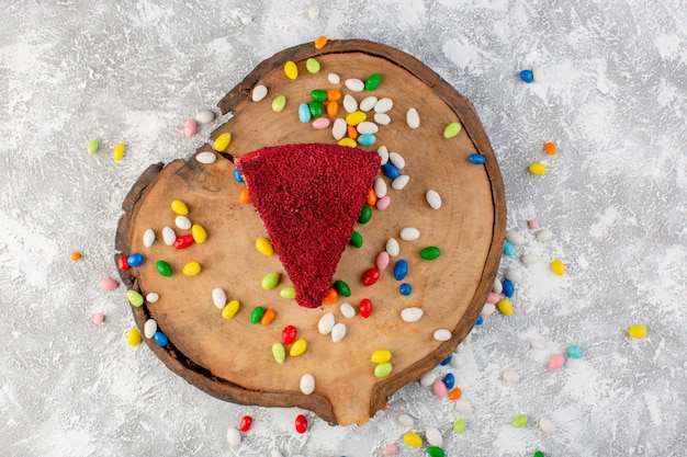 Вид сверху вкусный кусочек торта со сливками и фруктами на деревянном столе с разноцветными конфетами, бисквитными сладкими конфетами