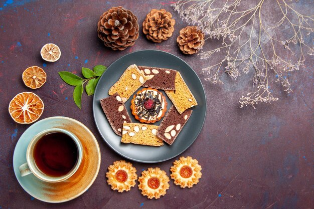 Top view delicious cake slices with little biscuit and cup of tea on a dark background biscuit cookie dessert cake tea sweet