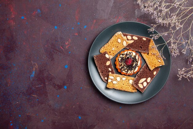Вид сверху вкусные кусочки торта с орехами и маленьким бисквитом на темном фоне, печенье, десерт, торт, сладкий чай