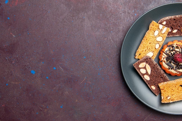トップビュー暗い背景にナッツと小さなビスケットのおいしいケーキスライス甘いビスケットクッキーデザートケーキ