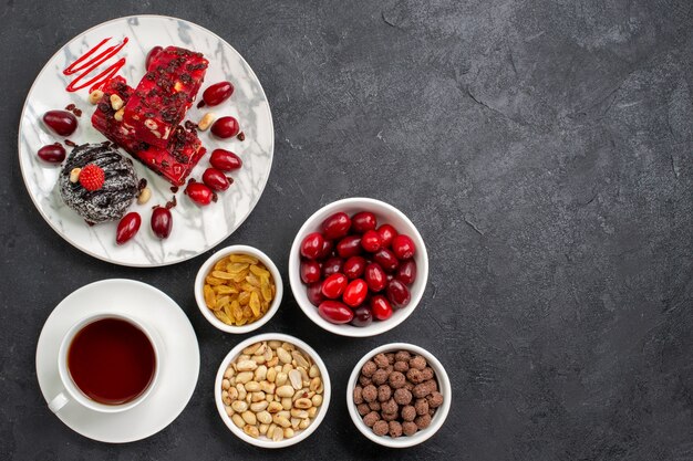 Top view delicious cake slices with nuts tea and dogwoods on grey desk